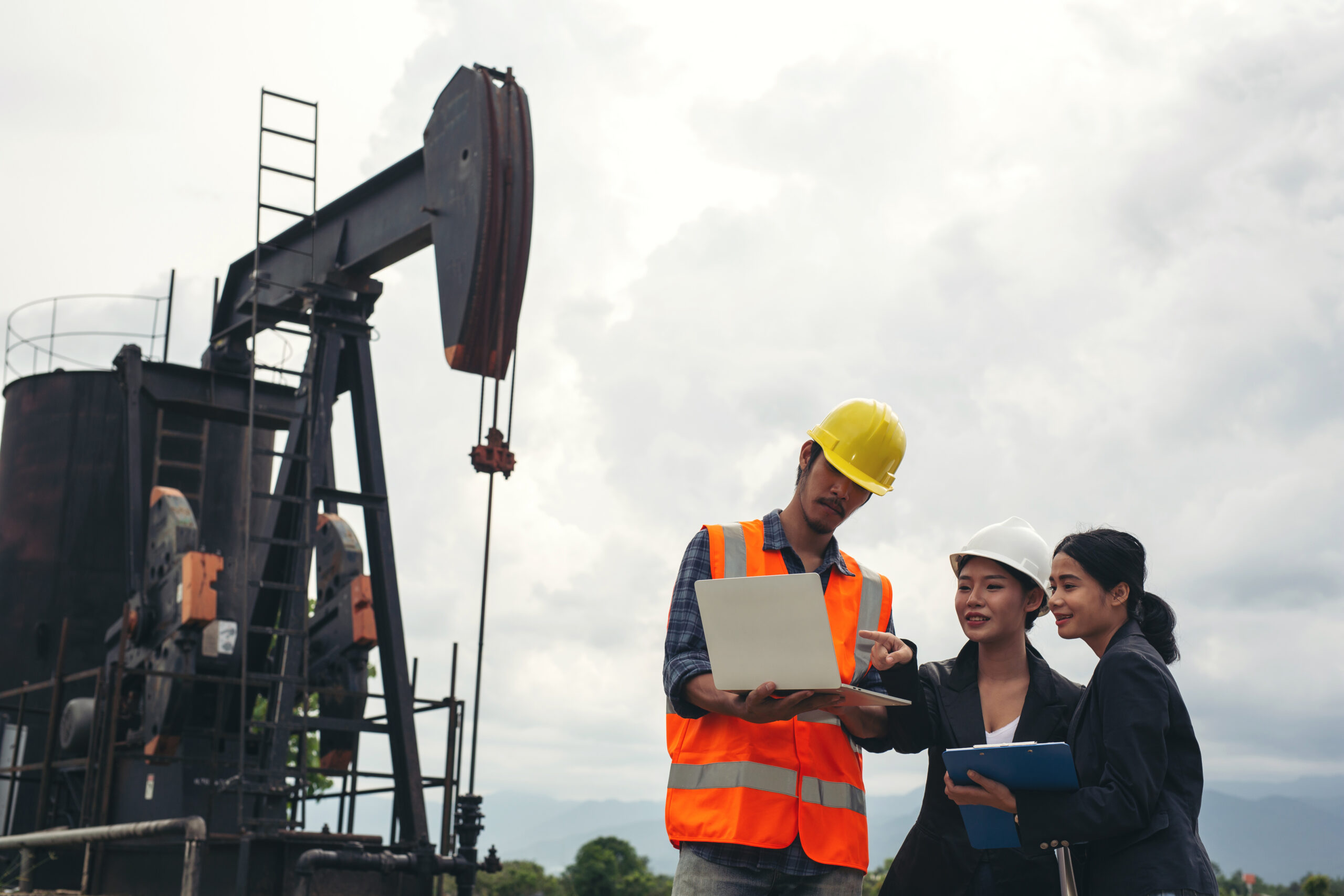 Engineering Team Stands Beside Working Oil Pumps With Sky Scaled
